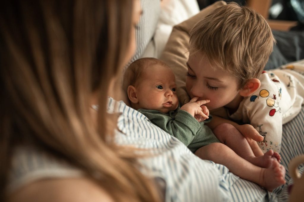 A heartwarming moment as a young child embraces a newborn sibling with mother nearby.